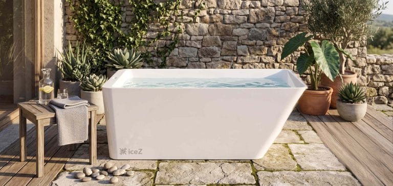 Modern white acrylic ice bath outdoors with plants and stone wall.